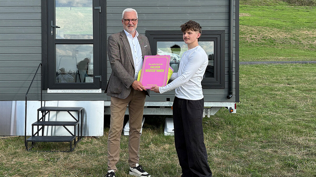 Der neue Haldenwärter Fynn, rechts, aus Hamburg bekommt das Buch der Haldenwärter*innen von Garrelt Duin, dem Regionaldirektor des RVR übergeben.