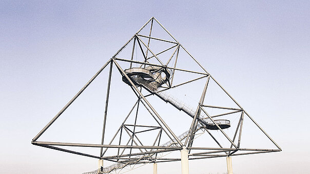 Gesamtansicht der pyramidenförmigen Stahlskulptur des Tetraeders in Bottrop. Die komplexe Konstruktion mit ihren begehbaren Treppen und Plattformen hebt sich als Landmarke klar vom hellen Himmel ab.