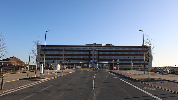Frontalansicht eines mehrstöckigen, modernen Bürogebäudes mit dunkler Fassade bei klarem, blauem Himmel auf dem Gelände von MARK 51°7.. 