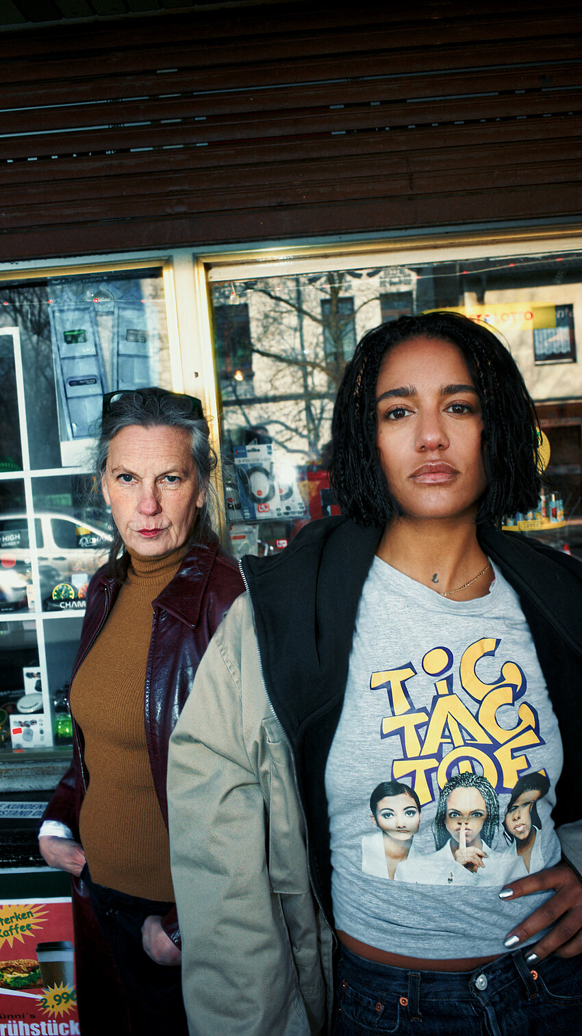 Die Protagonistinnen Horst (rechts) und Berta (links) stehen selbstbewusst vor einem Kiosk. Horst trägt ein T-Shirt mit Tic-Tac-Toe-Aufdruck, Berta eine Lederjacke.