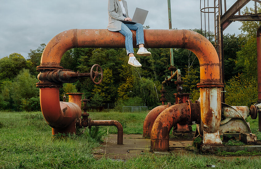 Eine Person sitzt mit Laptop auf einem Rohr auf dem Gelände der Zeche Zollverein.