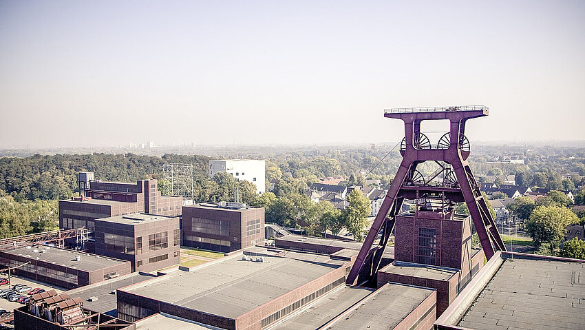 Panoramablick über die Zeche Zollverein in Essen. Das rote Fördergerüst und die historischen Zechengebäude prägen die weite Landschaft des Ruhrgebiets. Ein Symbol der Industriekultur.
